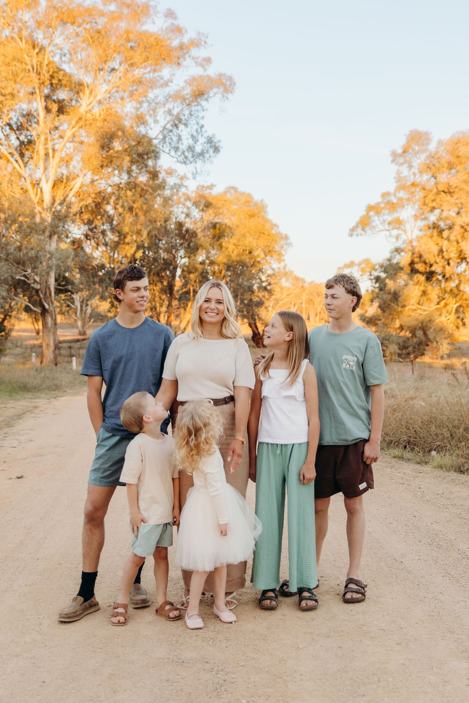 A mother poses with her four children on a golden dirt road surrounded by Australian eucalyptus trees at sunset.