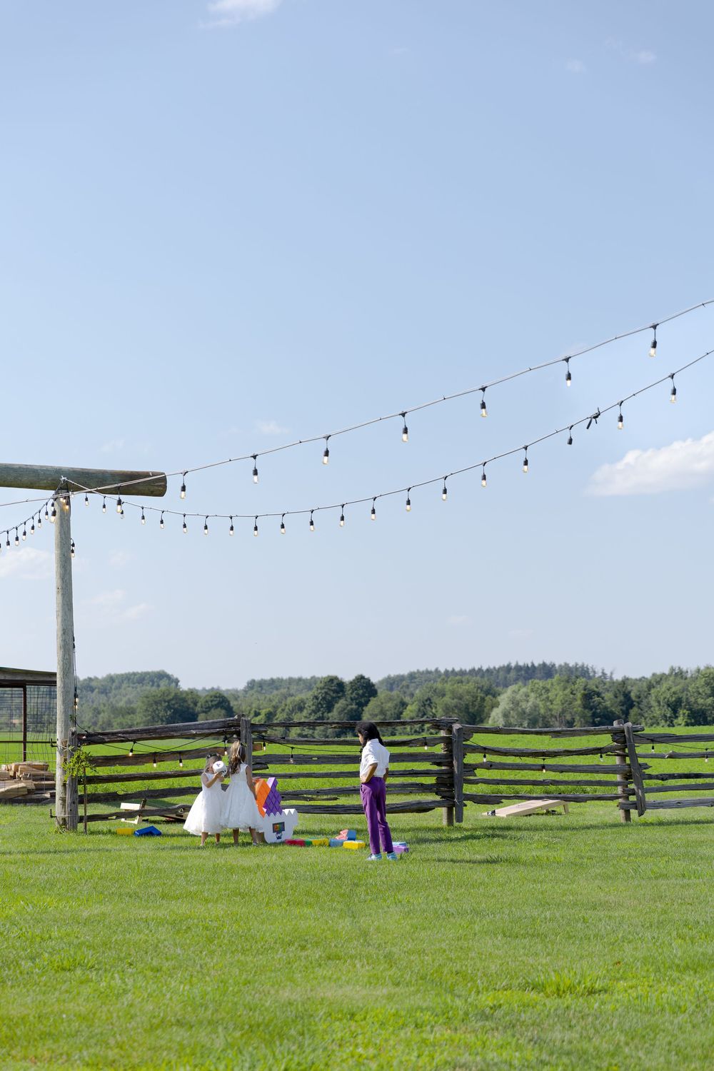 Outdoor farm wedding with string lights, rustic wooden fence on green grass under clear blue sky at barn swallow fields in guelph, ontario.