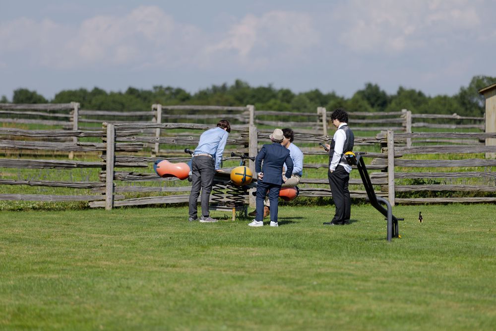 Kids playing on structure in green grass field with wooden split-rail fence at barn swallow fields in guelph, ontario.
