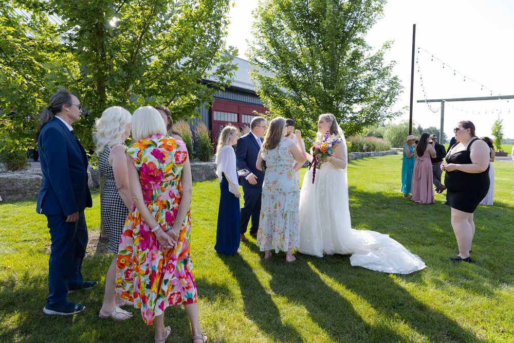 Outdoor wedding ceremony with bride and groom surrounded by guests on green lawn at barn swallow fields in guelph, ontario.