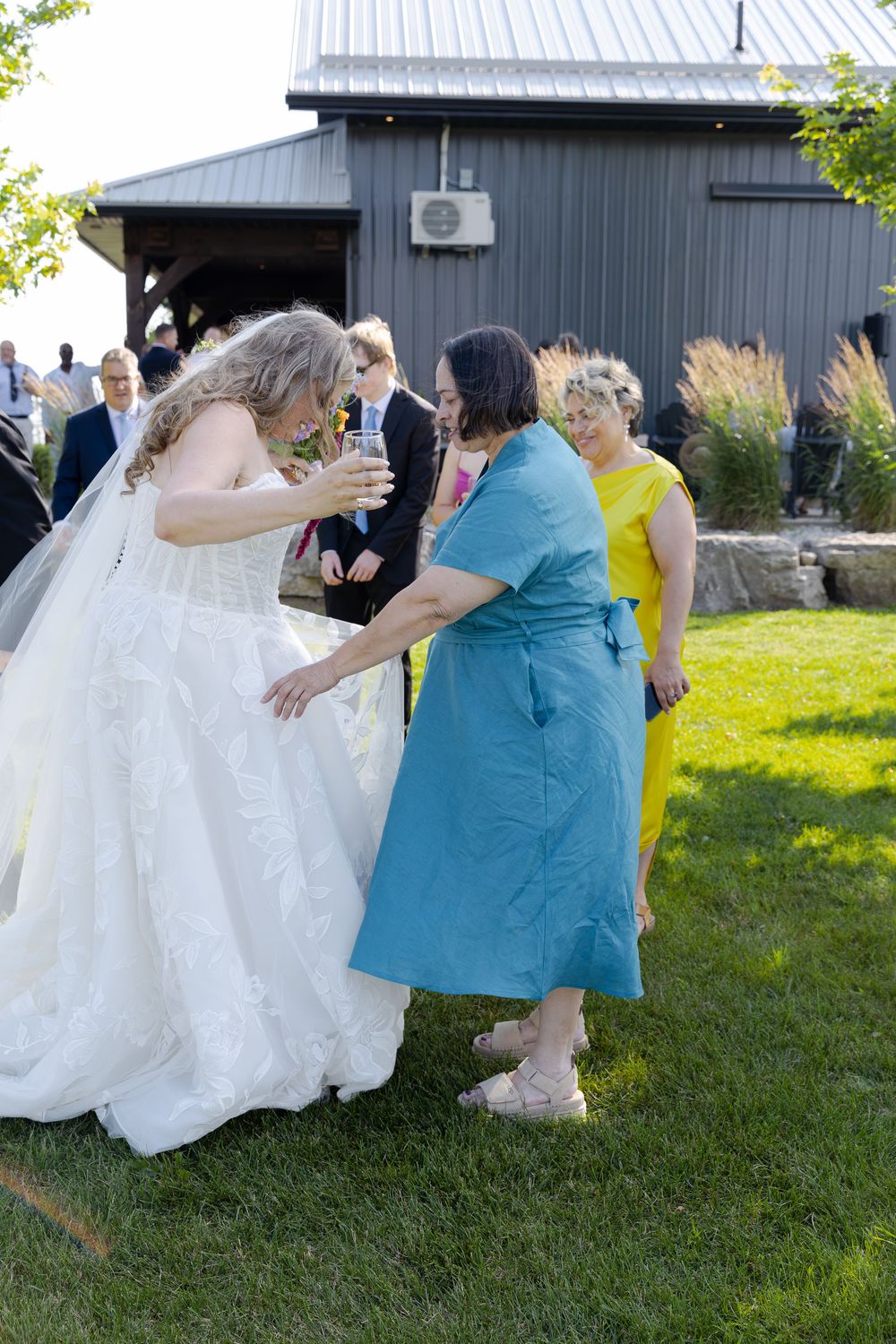 Bride in white gown interacts with guest in teal dress at outdoor wedding reception at barn swallow fields in guelph, ontario.