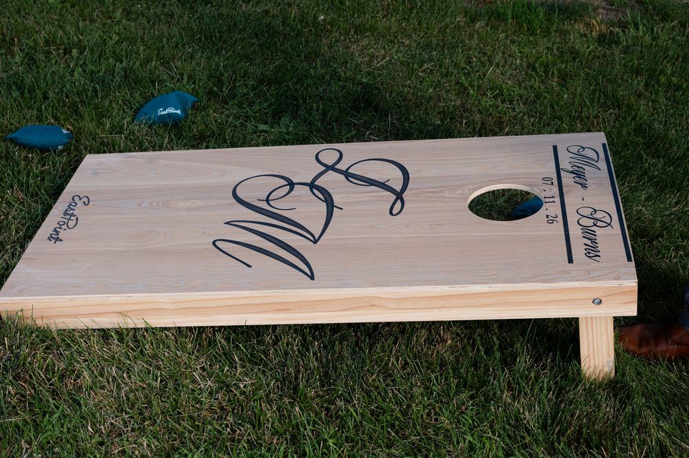 Custom engraved wooden cornhole board with signatures on green grass outdoors at barn swallow fields in guelph, ontario.