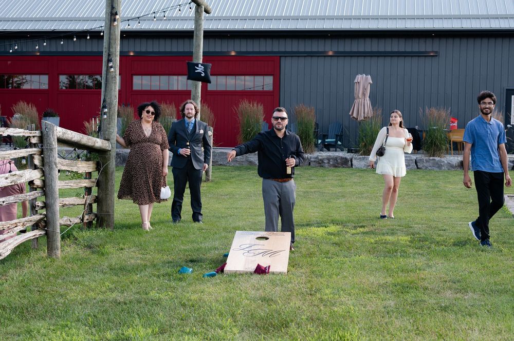 Group of friends playing cornhole lawn game outside at outdoor wedding at barn swallow fields in guelph, ontario.