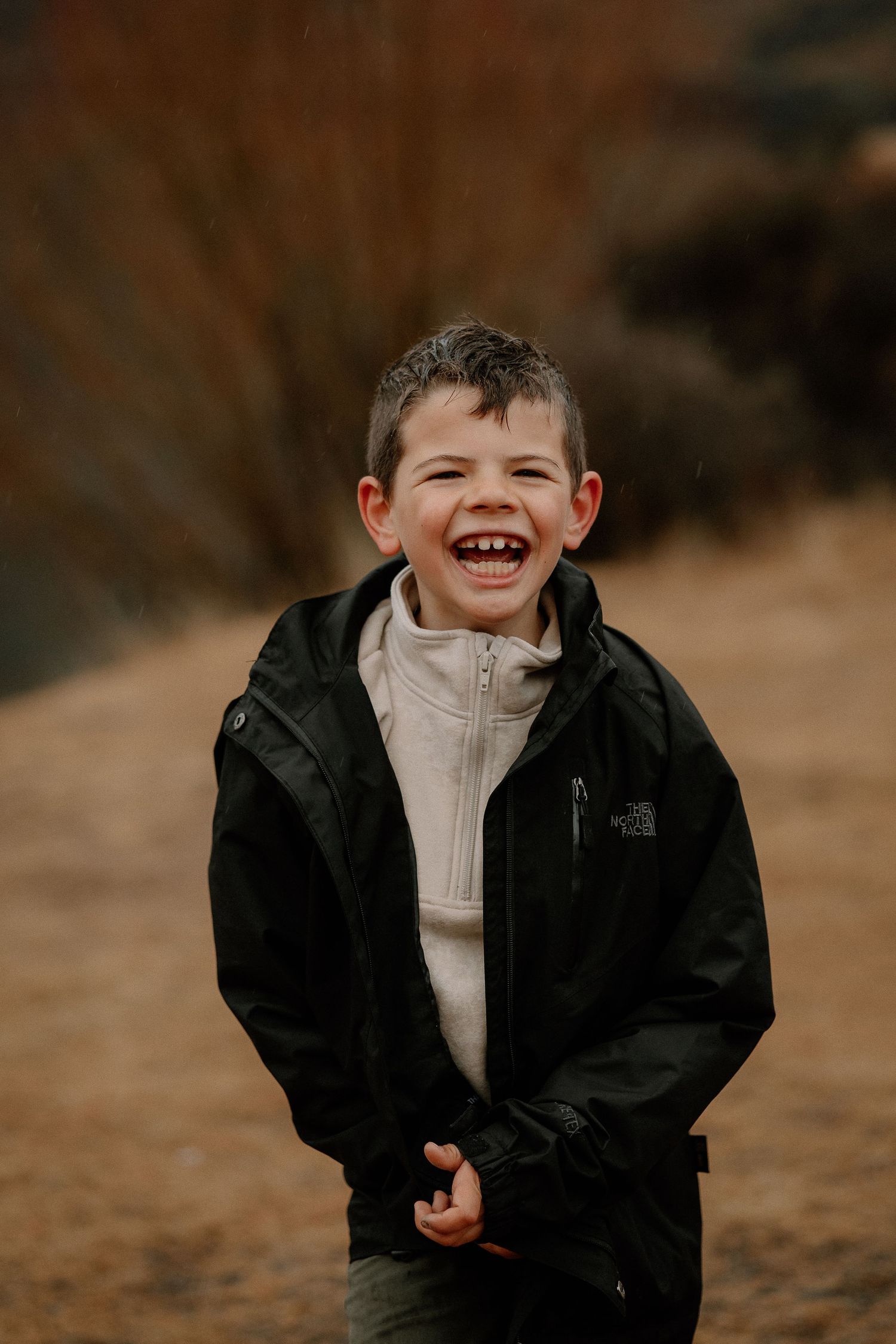 A laughing young boy wearing a black North Face jacket over a white fleece outdoors.