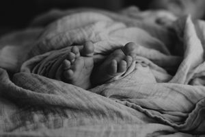 Black and white close-up of newborn baby feet wrapped in soft muslin cloth.