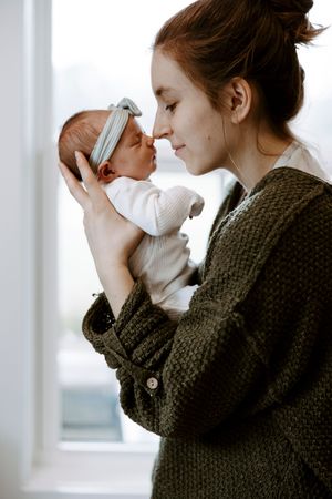 A young mother tenderly holds her newborn baby close, touching noses in a gentle moment of bonding.