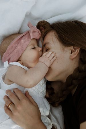 A mother with a braid tenderly touches foreheads with her newborn baby wearing a pink bow headband.