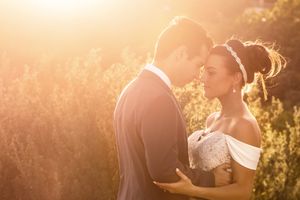 A bride and groom share a romantic moment in golden sunlight, surrounded by lush greenery on their wedding day.