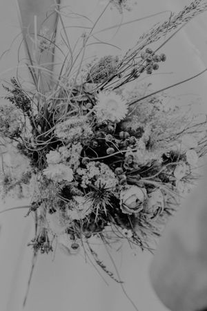 Black and white photo of a wild rustic bouquet with roses, berries, and dried grasses held by a bride.