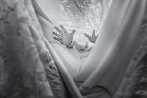 Black and white photo of hands pressed against sheer white curtains, creating a dramatic and ethereal effect.
