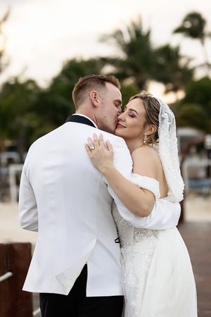 Bride and groom share a romantic kiss outdoors at a tropical wedding venue, with palm trees in the background.