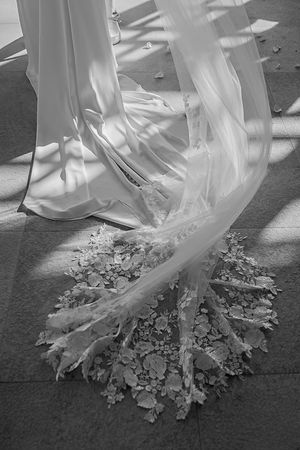 Black and white photo of a bride's lace cathedral veil and wedding dress train on stone floor.
