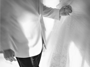 Black and white photo of a bride and groom holding hands, showcasing wedding attire and bridal veil.