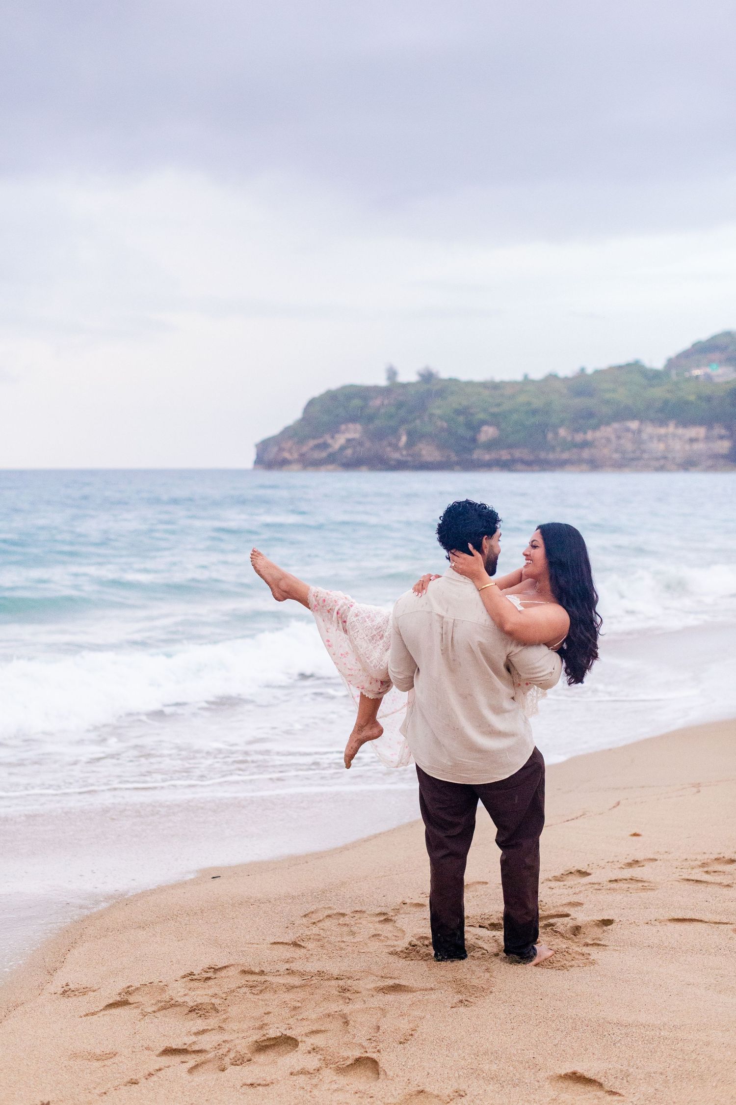 Engagement portrait on the beach. Man carrying woman at the water's edge. Playa Guajataca, Isabela, Puerto Rico.