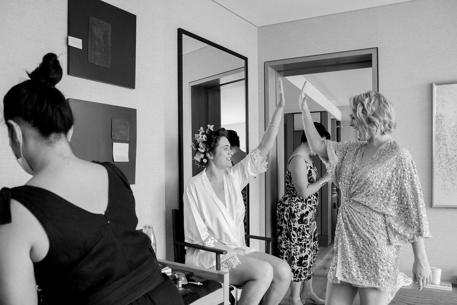 Bride and bridesmaid celebrate in mirror reflection during wedding preparations in black and white photo.