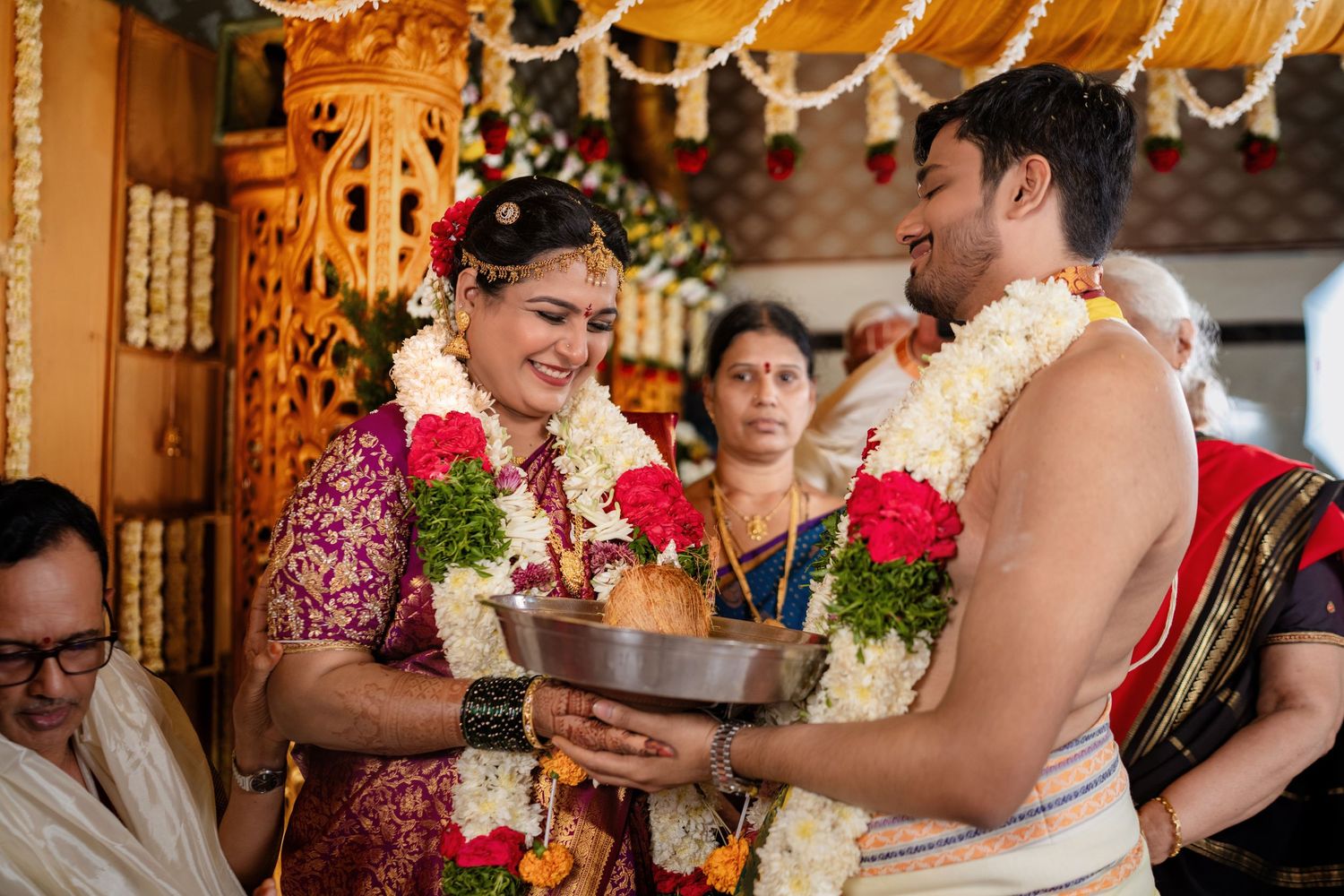 Bride and groom exchanging garlands during a traditional South Indian Hindu wedding ceremony with floral decorations.