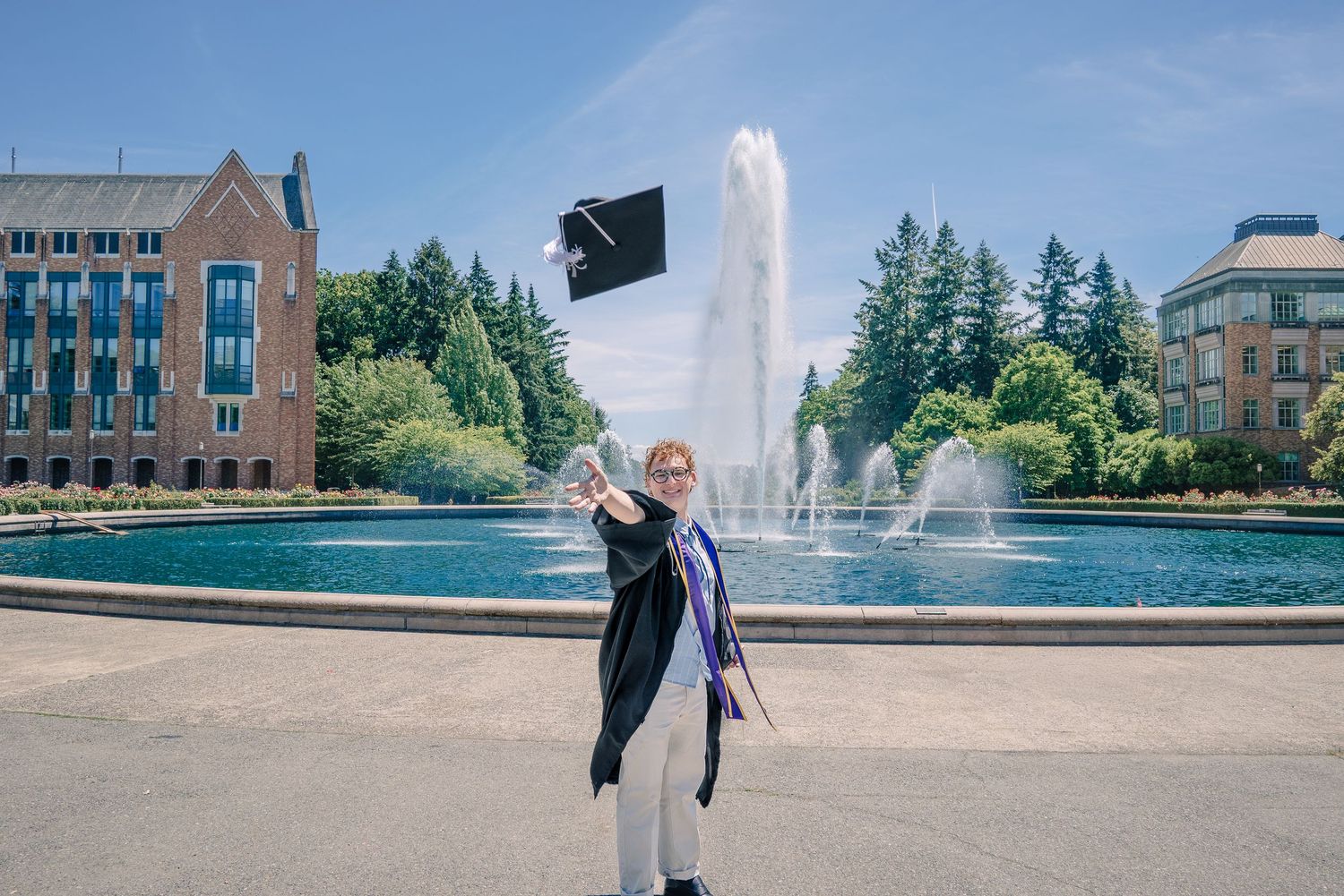 University of Washington graduate smiling near Drumheller Fountain with a cap toss