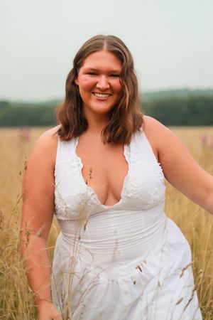 Person in white summer dress poses joyfully in tall grass field.