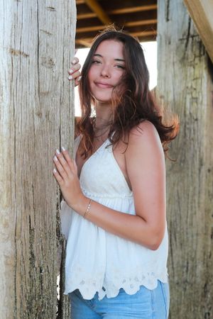 Playful portraits between wooden pier posts in casual summer attire.