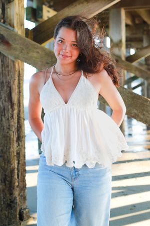 Casual summer photos under a pier wearing light denim and a white ruffle top.