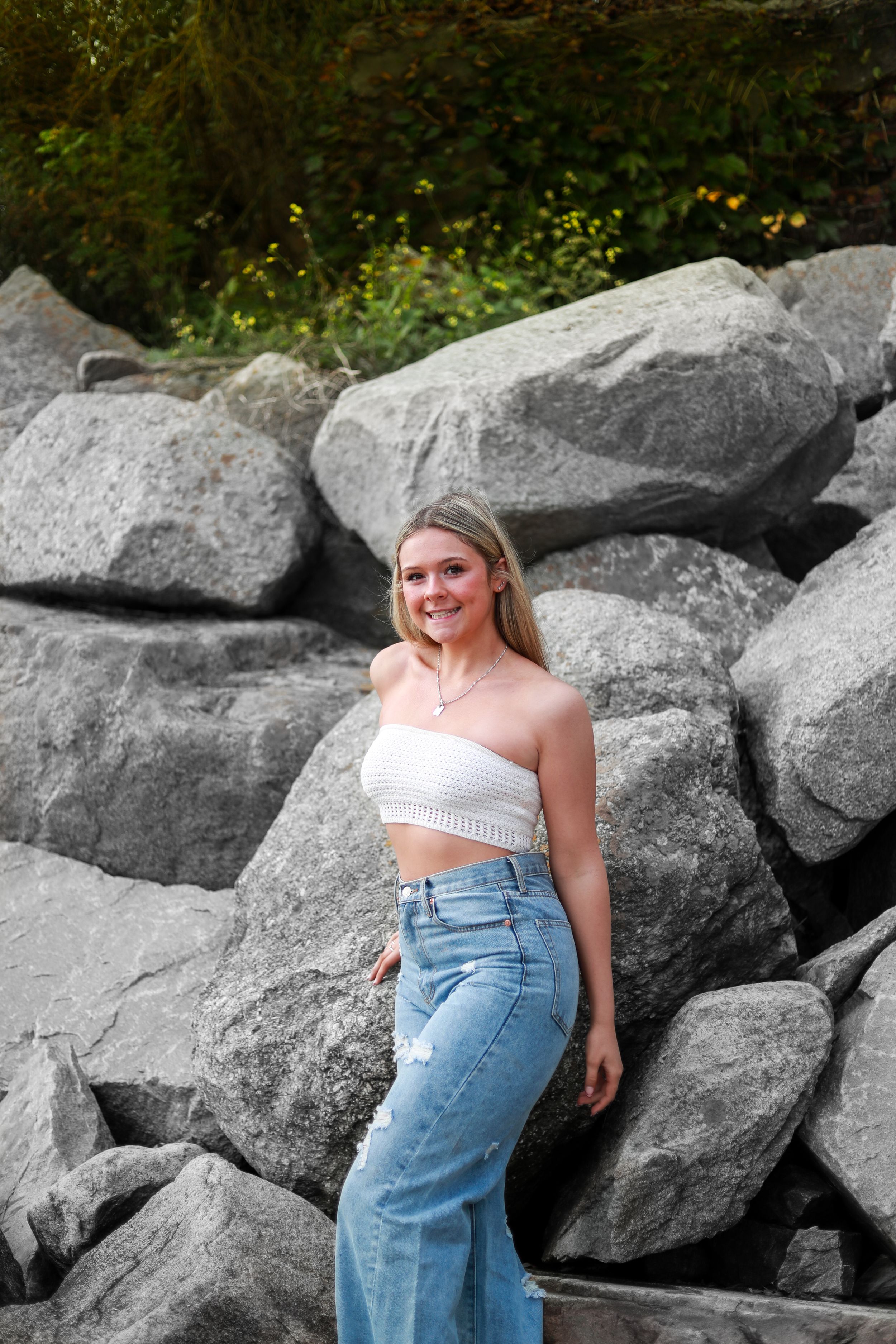 A casual portrait against large rocks with someone wearing high-waisted jeans and a white crop top.