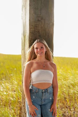 Person in white crop top and jeans poses against sunlit wooden backdrop.