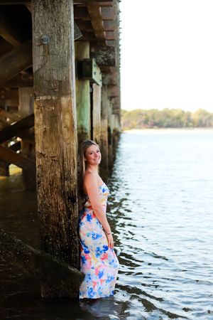 A scenic photo under a pier with someone wearing a floral dress standing in shallow water.