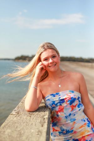 Woman in colorful floral dress poses on concrete wall by waterfront.