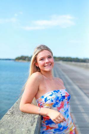 A seaside portrait with someone in a blue and orange patterned dress leaning on a wooden railing.