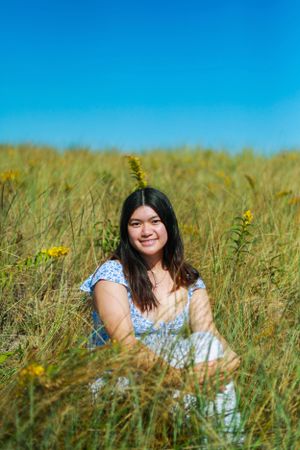 Person in blue floral dress lying in field of yellow wildflowers under bright blue sky.