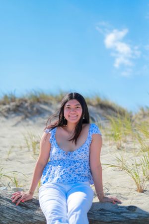 Person wearing blue floral top and white pants poses on sandy beach dunes.