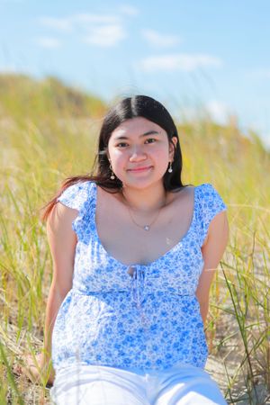 Person in blue floral dress sitting on beach sand with dune grass in background.