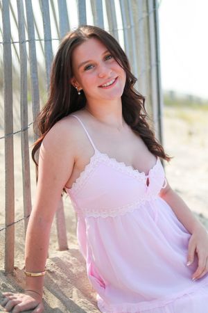 Person in white sundress poses between wooden beach fence posts.
