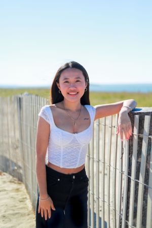 Person in casual summer outfit poses cheerfully by beach fence with ocean view.
