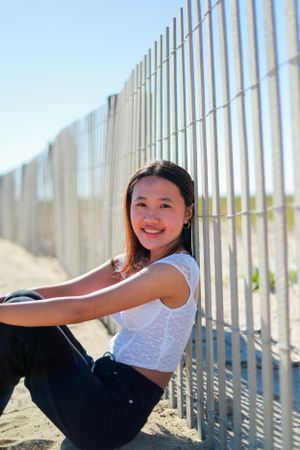 Person in white crop top and dark pants poses by wooden beach fence.