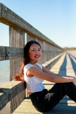 A casual portrait taken on a wooden boardwalk with someone sitting against the railing.