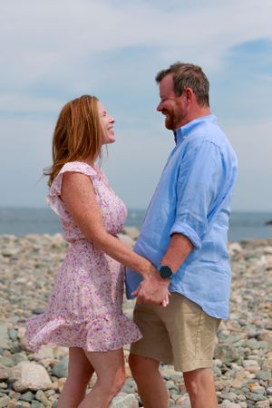 Couple in casual beach attire sharing playful moments on rocky shoreline.