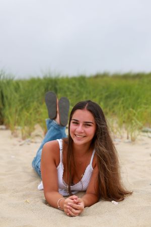 Person in casual white top and jeans lying on beach sand during summer photoshoot.