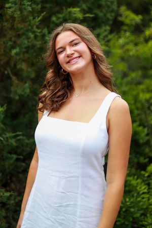 Portrait of person in white dress outdoors with green foliage background.