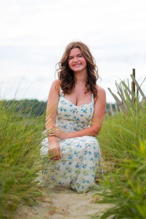 A summer photoshoot in tall grass featuring a floral blue sundress against a cloudy sky.