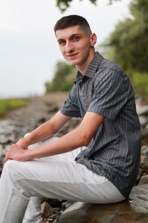 A person in grey shirt and white pants sits on rocky terrain outdoors.