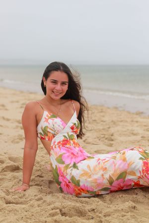 A person in a floral dress relaxes on the sand at a peaceful beach.