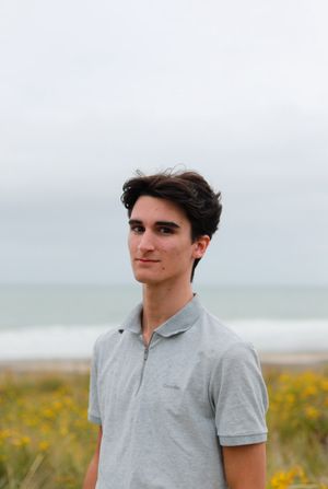 Person in grey polo shirt poses in front of coastal scenery with yellow wildflowers.