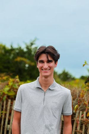Person in grey polo shirt poses outdoors near wooden fence.