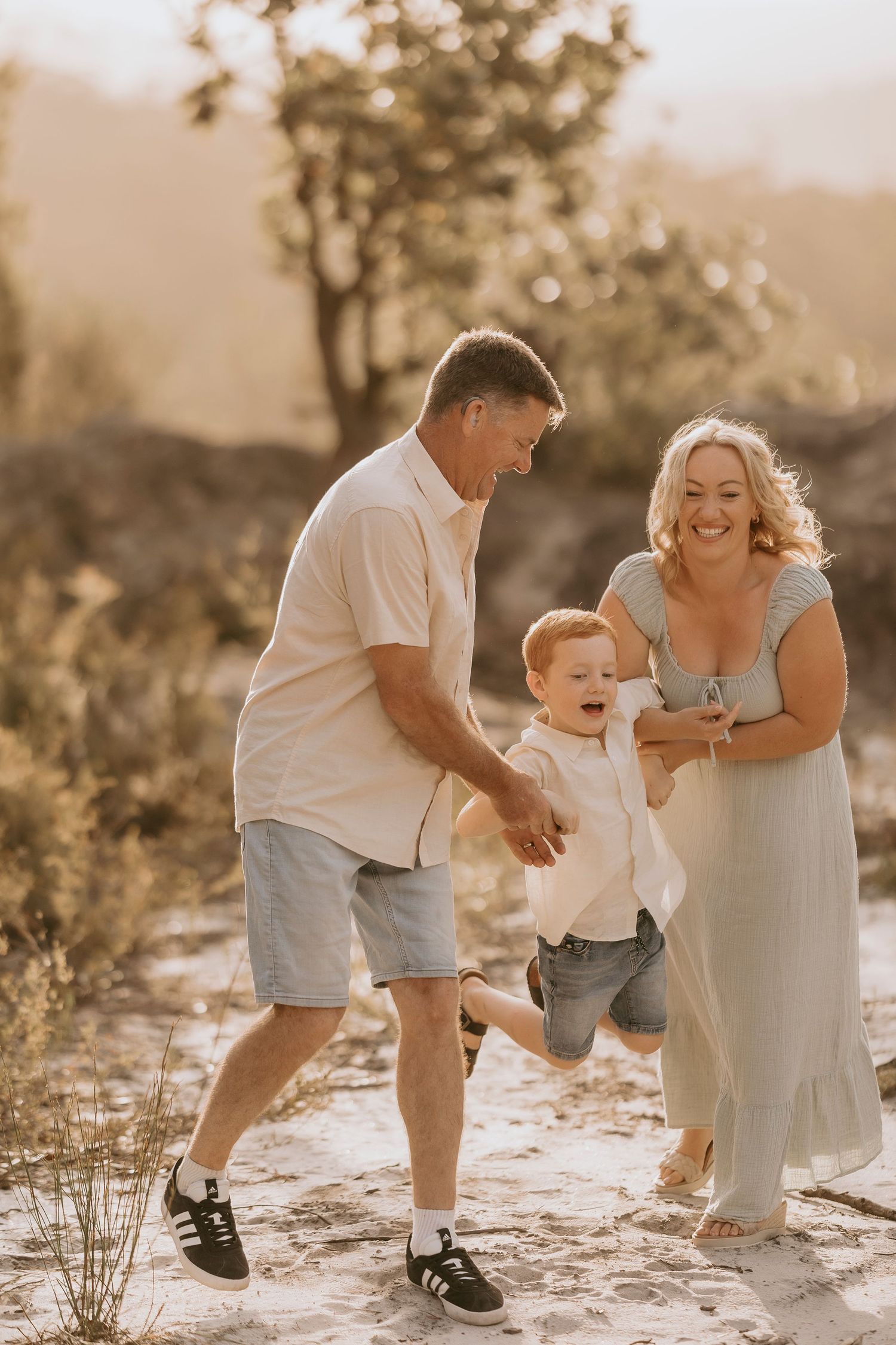 Family of four sitting on rocky beach at golden sunset with lush green hillside backdrop.