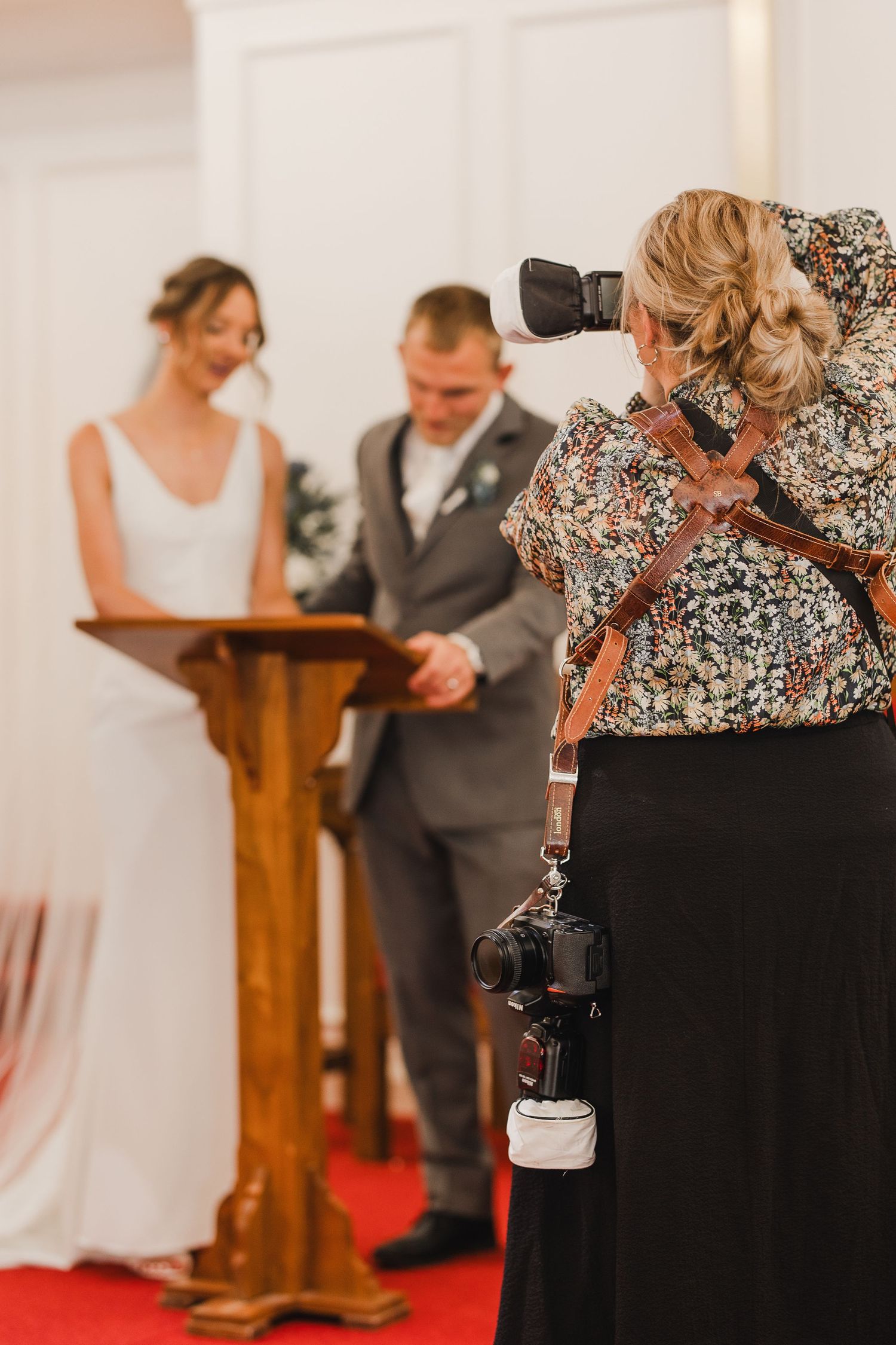 Wedding photographer capturing bride and groom exchanging vows at altar during indoor ceremony.