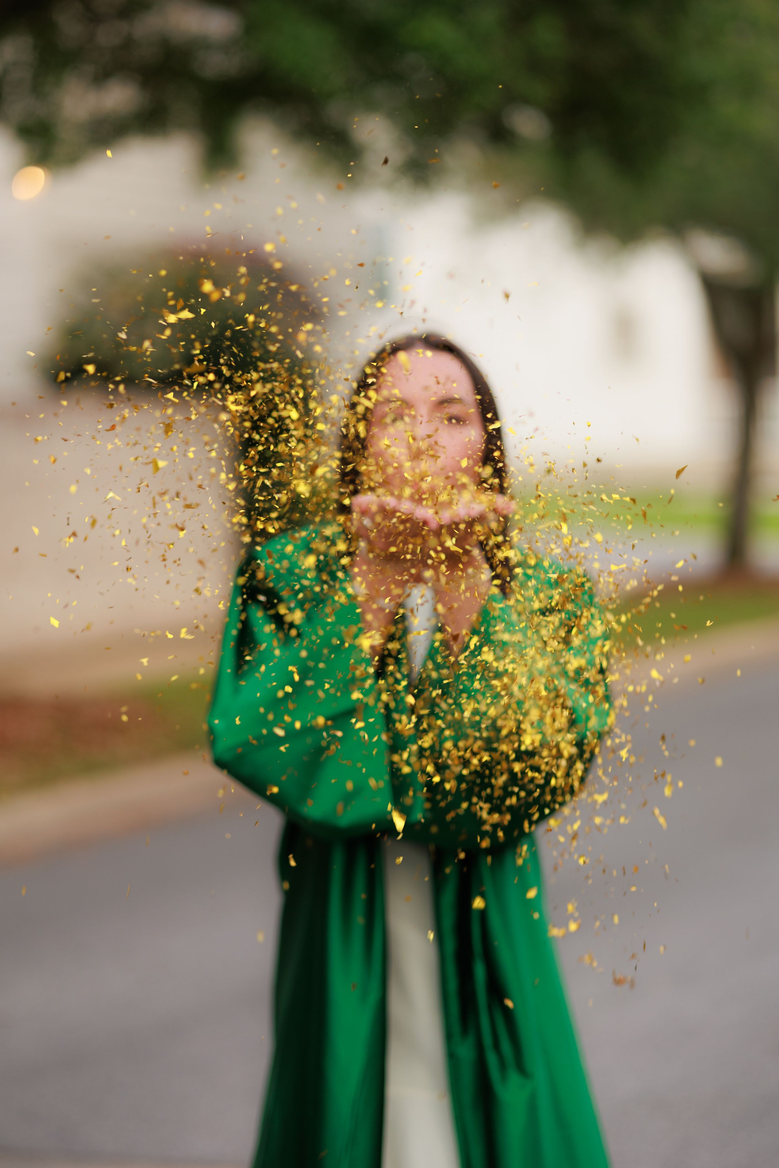Woman in green dress blowing gold confetti outdoors.