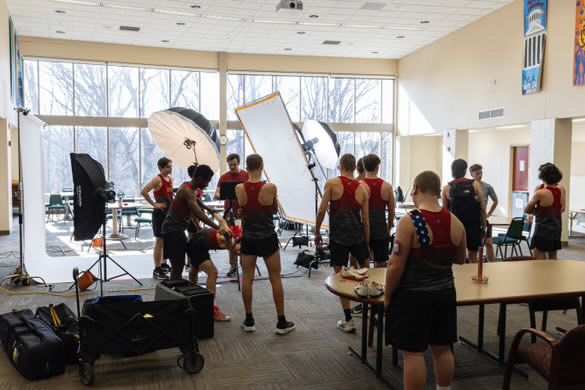 Athletes in red uniforms gather for a photo shoot with professional lighting equipment in a modern indoor facility.