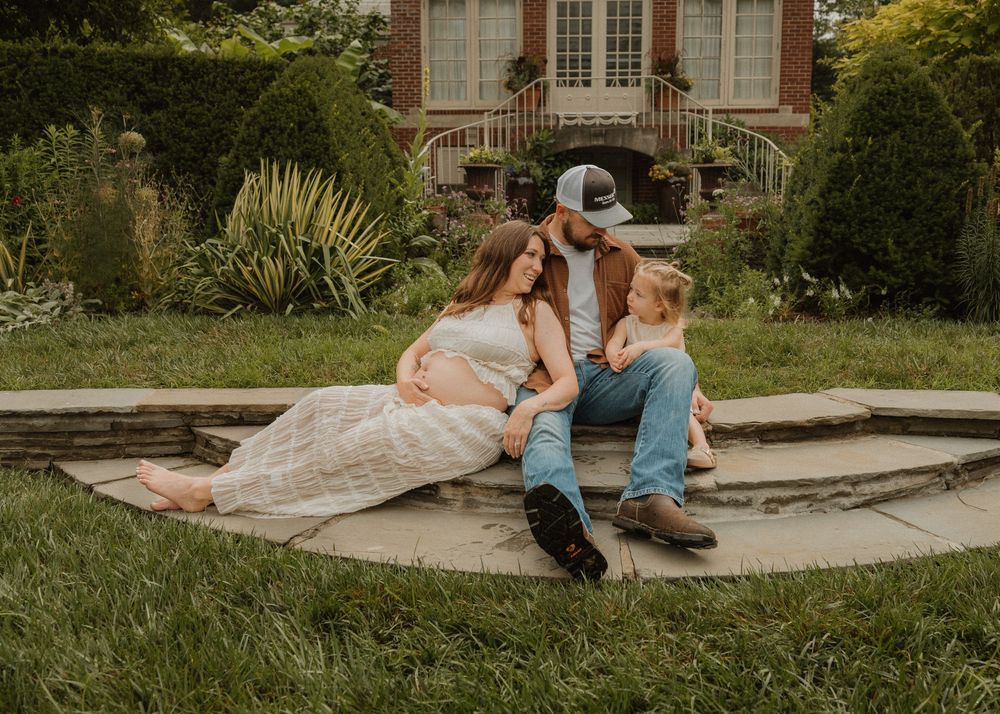 Maternity photo of expecting couple with child sitting on stone steps near historic building.