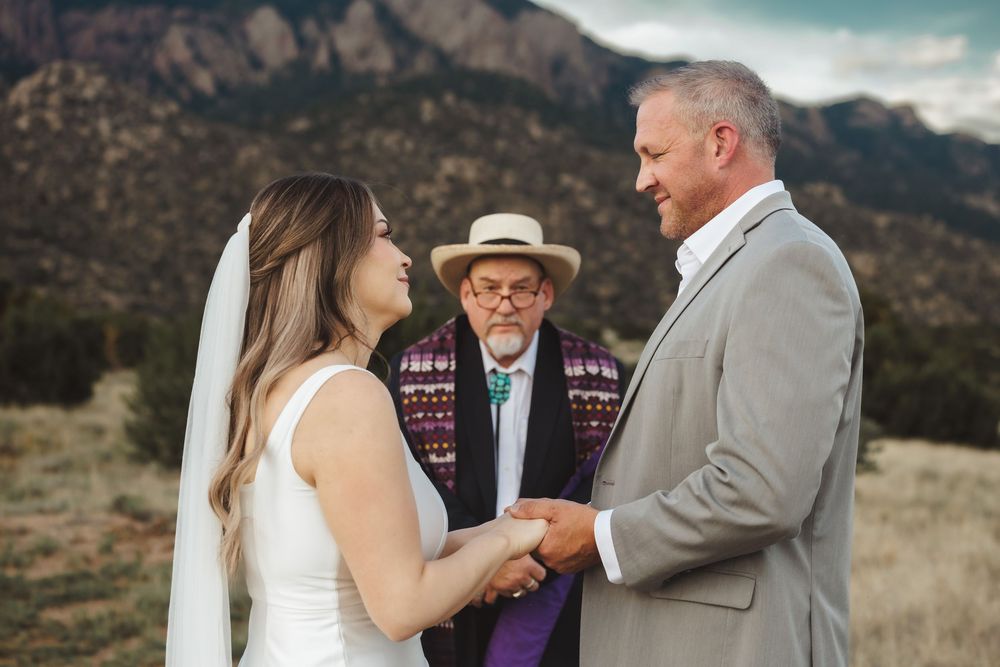 Couple exchanges vows with officiant in hat during outdoor mountain wedding ceremony in New Mexico.
